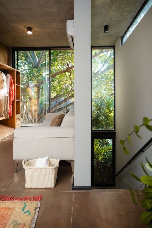 Bright modern living room with a beige sofa a woven basket on the floor and a clothing rack on the left glass doors reveal greenery outside