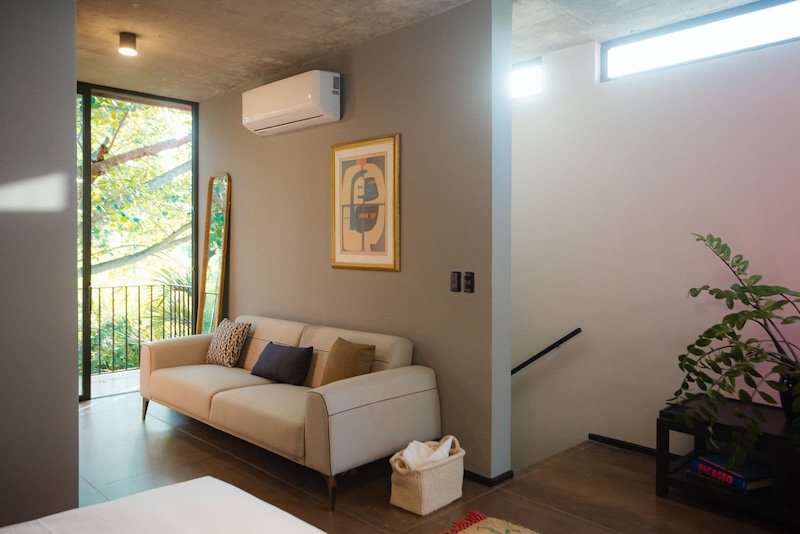 Beige sofa in a modern living room with abstract artwork a wall air conditioner and a balcony door nearby