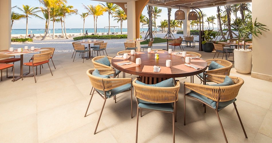 Outdoor beachside restaurant with a round wooden table and wicker chairs palm trees and the ocean in the background