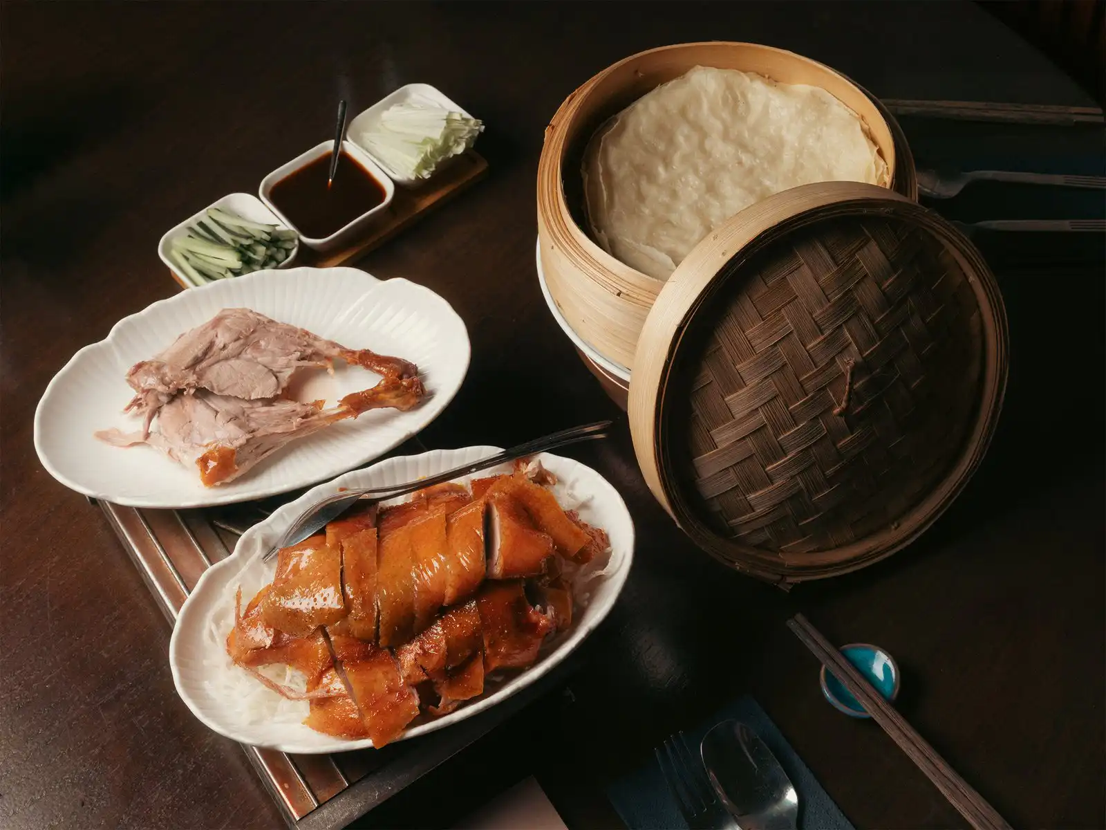 Chinois peking duck the hidden inn punta cana sliced roasted duck on a white plate with cucumber sauce and a bamboo steamer nearby for a dim sum meal