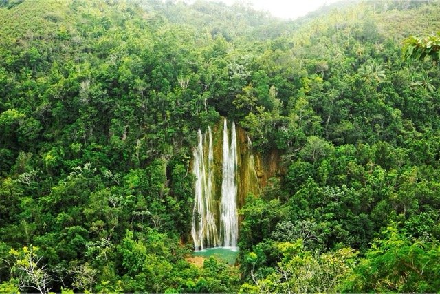 Waterfall cascading down a cliff into a turquoise pool surrounded by dense tropical forest park greenery