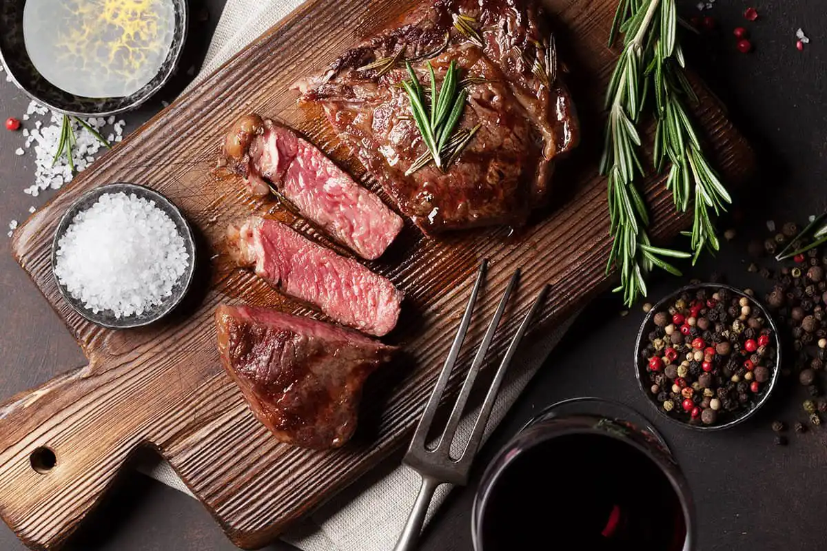 La tiendita meat the hidden inn punta cana sliced medium rare steak on a wooden cutting board with rosemary salt pepper and a glass of red wine nearby