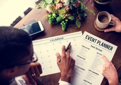 Top-down view of a calendar and an 'Event Planner' sheet being filled on a wooden table, with coffee and a smartphone nearby.
