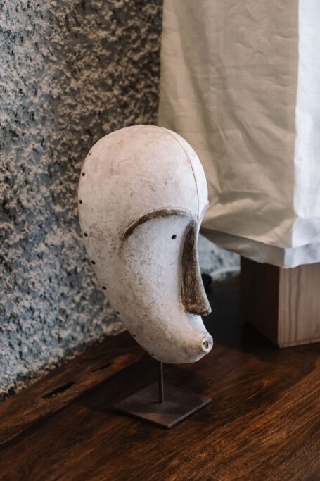 Casco medieval blanco y desgastado, expuesto en un soporte en el interior, con una pared texturizada al fondo