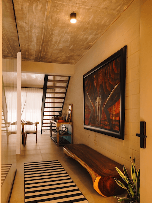 el vestíbulo de una vivienda moderna, con un banco de madera, un cuadro de gran tamaño y una escalera que conduce a la planta superior