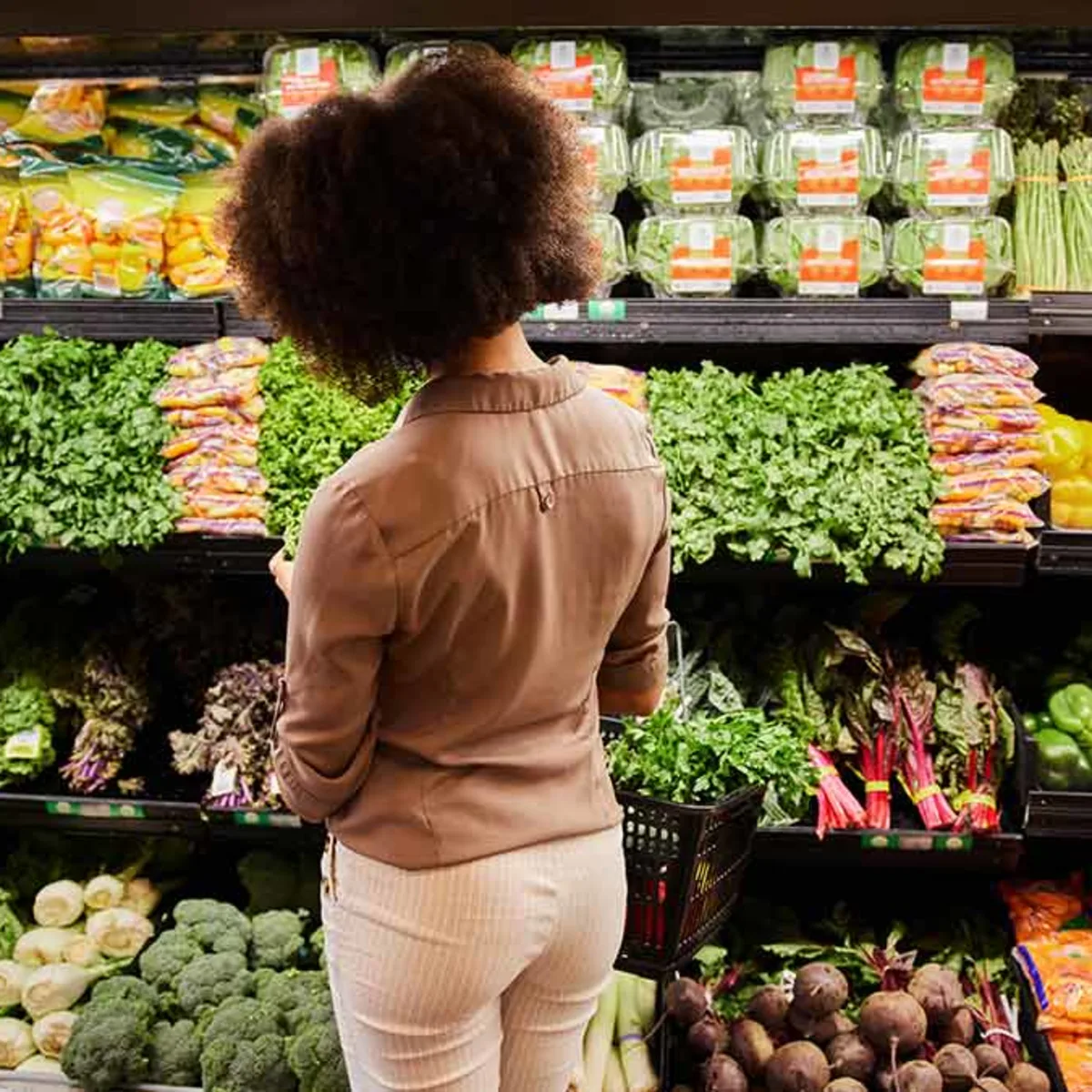 Grocery shopping the hidden inn punta cana back view of a woman with curly hair selecting leafy greens in a grocery store produce section a shopping basket visible at her side