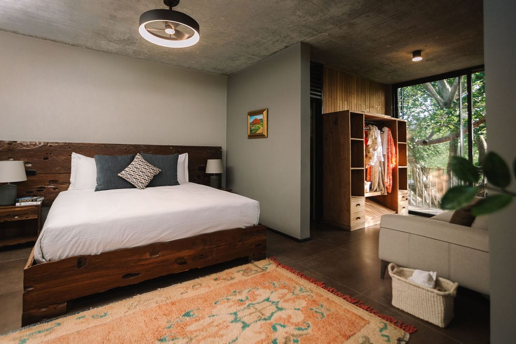 Private loft bedroom 2 the hidden inn punta cana hotel bedroom with a rustic wooden platform bed white linens gray walls and a colorful rug in the foreground