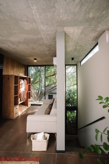 Private loft detail 3 the hidden inn punta cana modern living room with exposed concrete ceiling a wooden wardrobe on the left and a white sofa facing large windows revealing greenery outside