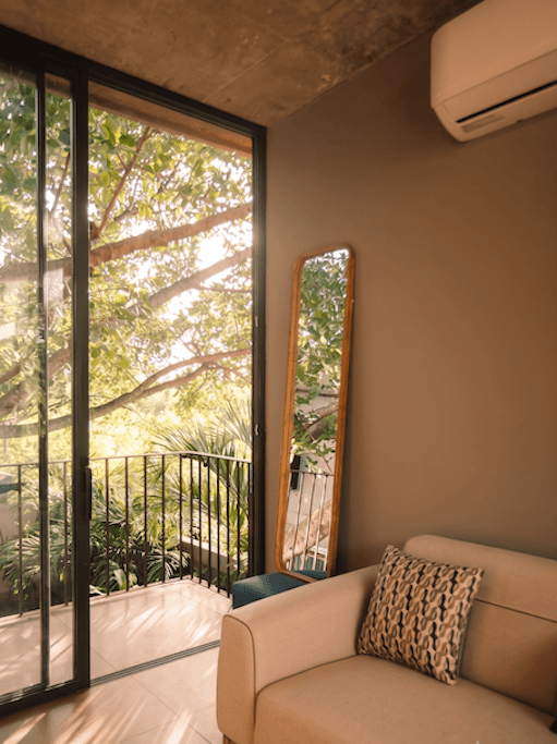 Private loft detail the hidden inn punta cana living room with a sliding glass door to a balcony greenery outside a tall mirror leaning against the wall and a beige sofa with a patterned cushion